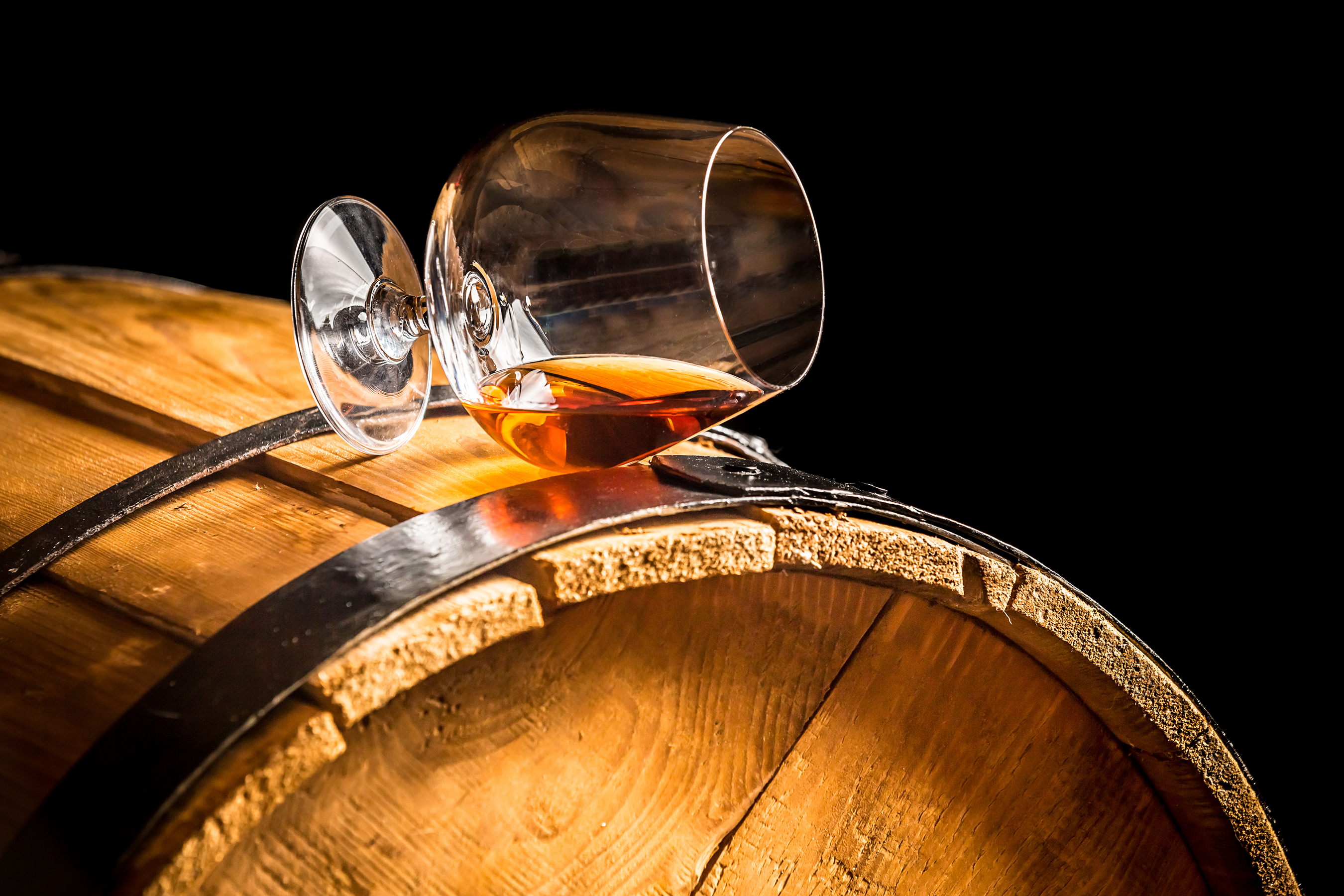 Ein liegendes, gefülltes Cognacglas auf einem Fass.