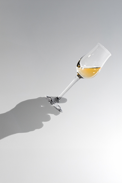 Ein gefülltes Schnapsglas, das von einer Schattenhand gehalten wird.